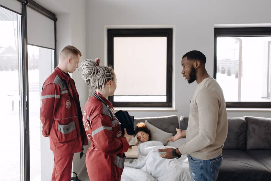 Paramedics assisting a patient at home, illustrating urgency and healthcare support indoors.